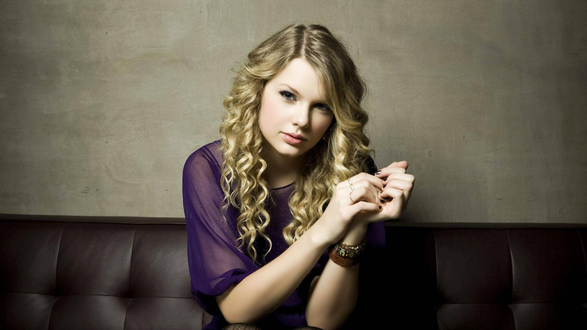 Ταπετσαρία με καθιστή Taylor Swift, σγουρά μαλλιά και μωβ διάφανο τοπ. — Taylor Swift Ταπετσαρία