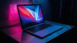 Ένα cyberpunk-inspired MacBook με αντανακλάσεις νέον σε σκοτεινό δωμάτιο.