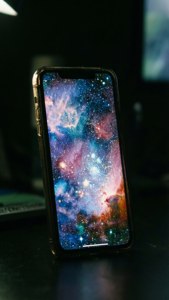 Οθόνη iPhone 17 να λάμπει με ταπετσαρία γαλαξία στο σκοτάδι.